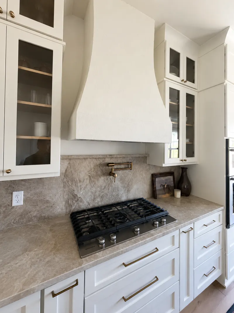 Plaster range hood over a gas cooktop with stone backsplash and pot filler